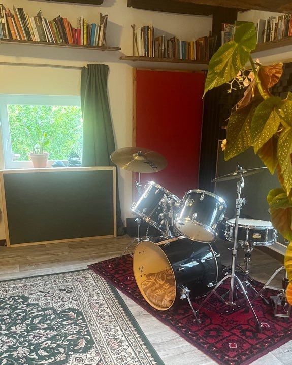 Drumset in der Studioecke mit rotem Akustikpanel und Pflanzen