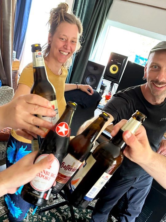 Helge und Max stoßen im Studio mit Bierflaschen an