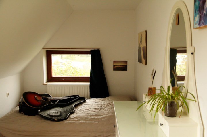 Schlafzimmer unter der Dachschräge mit Doppelbett, Gitarre und Blick ins Grüne