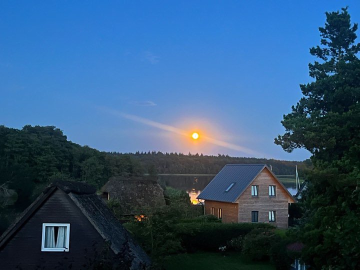 Abendhimmel mit leuchtender Scheibe über dem Schaalsee und Häusern am Ufer